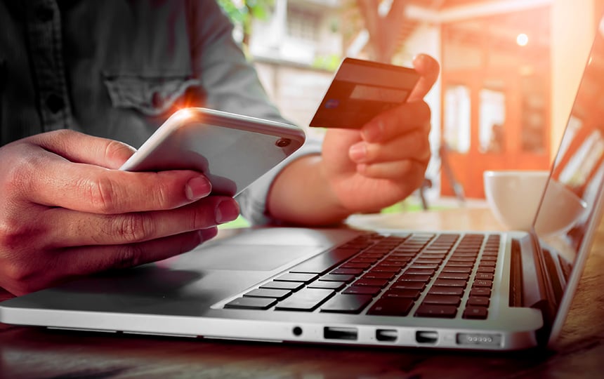 Homem com celular e cartão na mão fazendo uma compra no notebook 